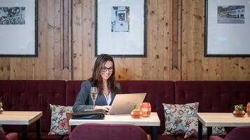 A person seated at a table with a laptop, a glass of water, and decorative items on a wooden wall with framed pictures.