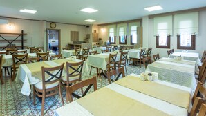 A dining area with multiple tables and chairs, a clock on the wall, and a window with curtains. - Hıdırlık Konakları (Safranbolu)