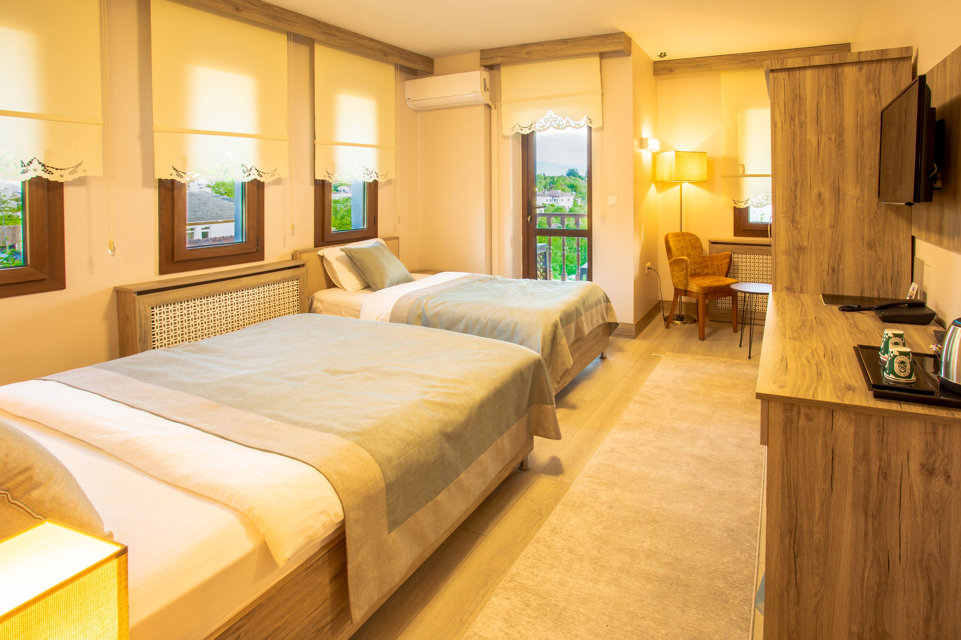 A hotel room with two beds, a desk, a chair, a TV, and a balcony with a view.