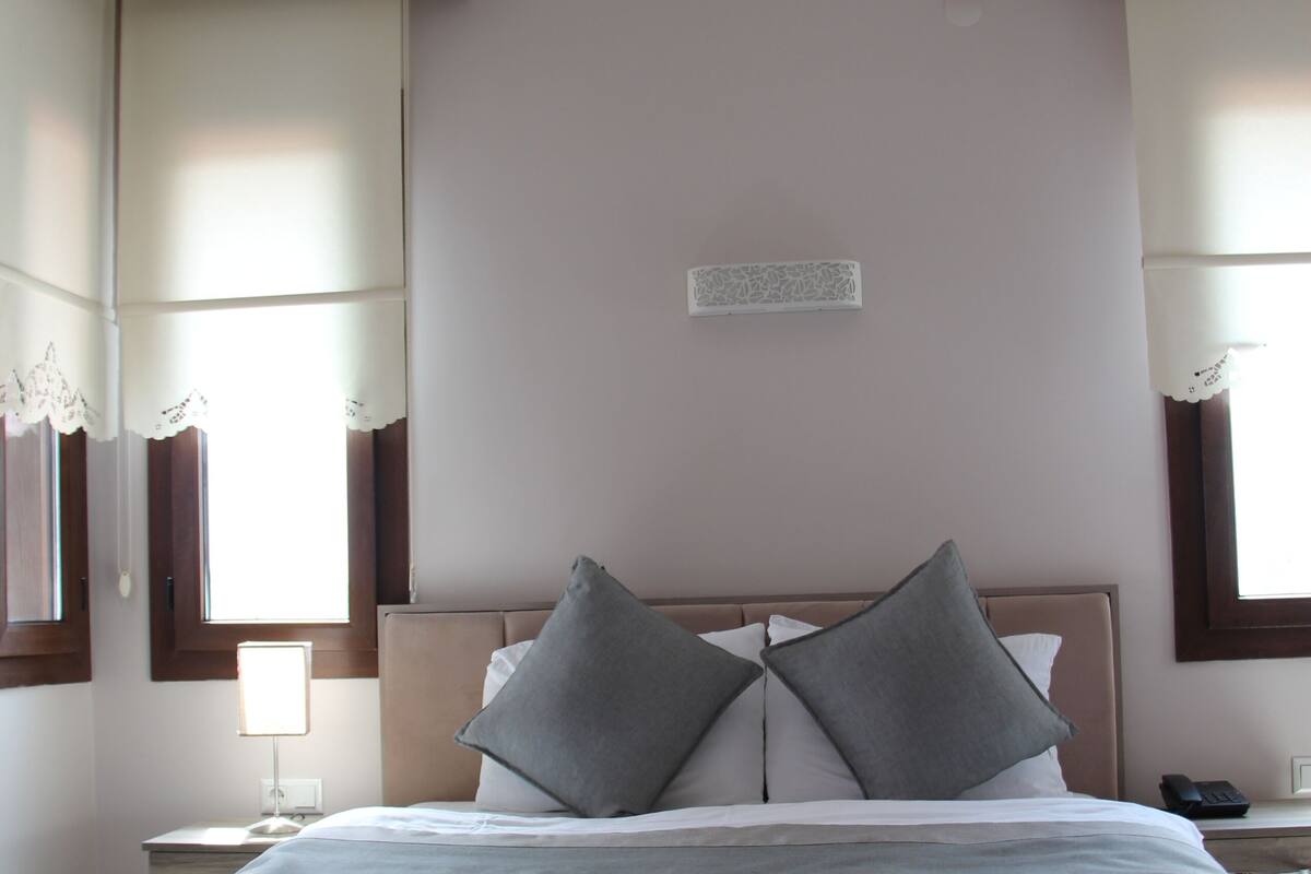 A neatly made bed with a headboard, two bedside tables, a nightstand, and a window with curtains.