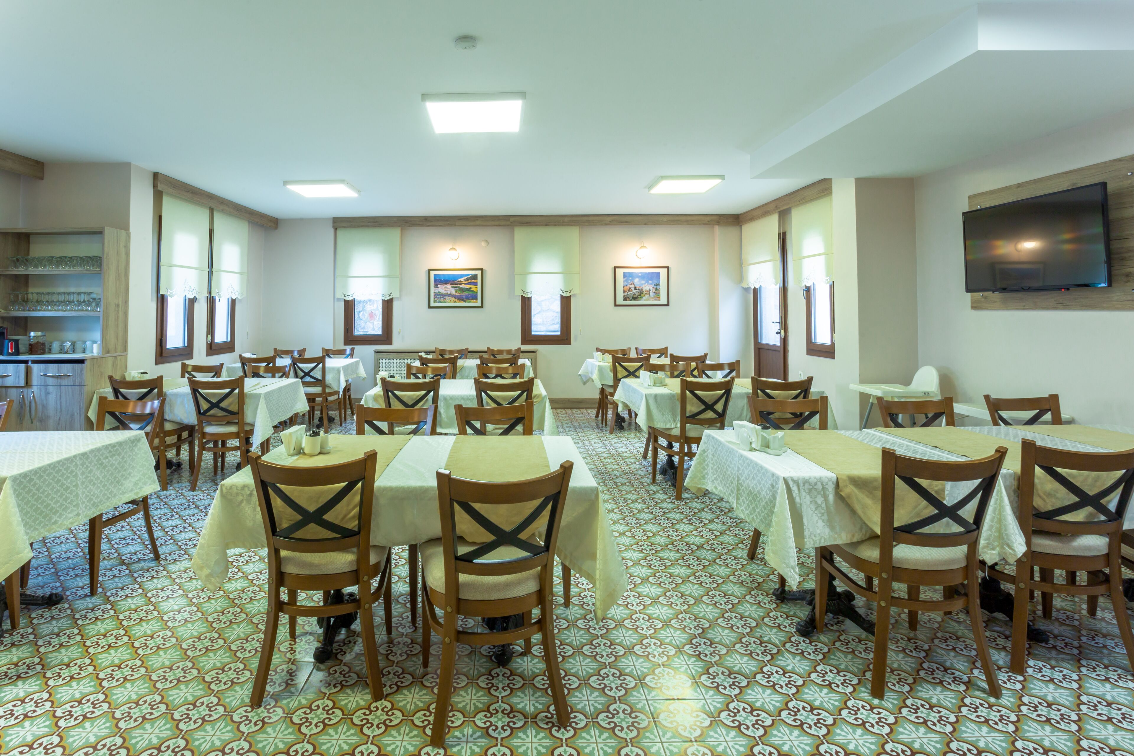 A dining area with multiple tables and chairs, tiled flooring, and wall-mounted artwork.
