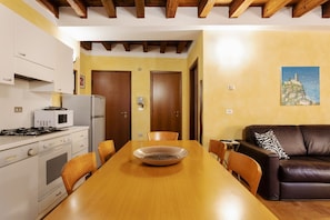 Une cuisine avec des appareils électroménagers blancs, une table à manger avec des chaises, un canapé en cuir marron et un tableau accroché au mur.