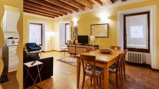 Un espace repas comprenant une table et des chaises en bois, un canapé, un téléviseur et des œuvres d’art accrochées aux murs.