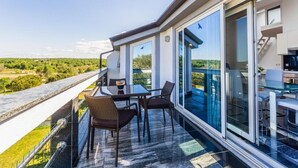 Een balkon met een tafel en stoelen, grote ramen en uitzicht op groen.