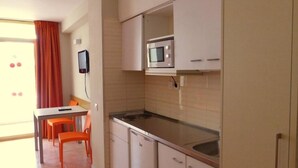 Een kleine keuken met een magnetron, een spoelbak en een eethoek met stoelen.