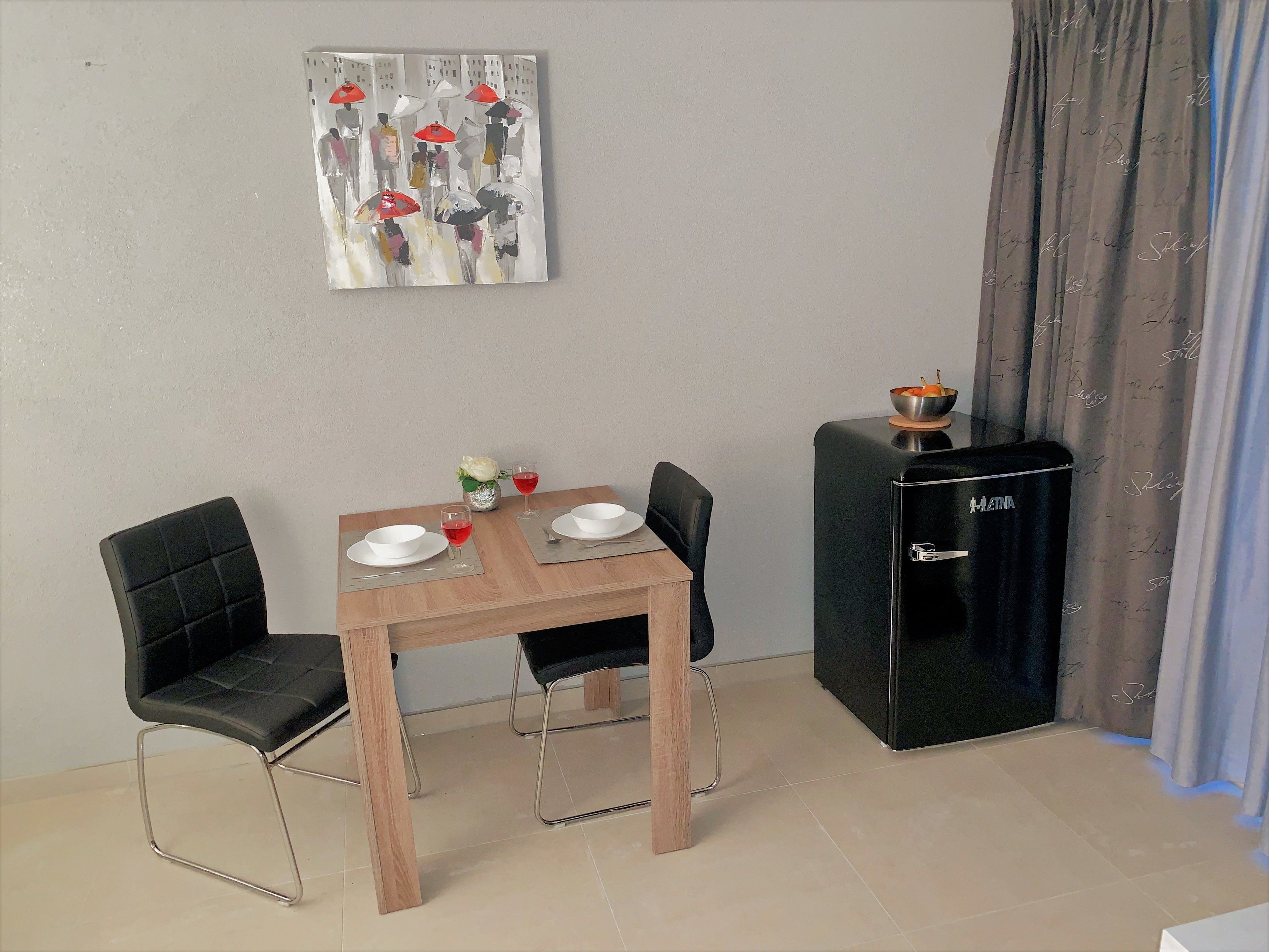 Un comedor con una mesa de madera, sillas negras y un refrigerador negro.