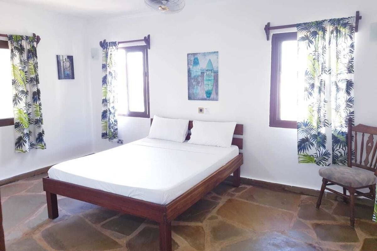 A bedroom with a bed, a chair, and a fan.