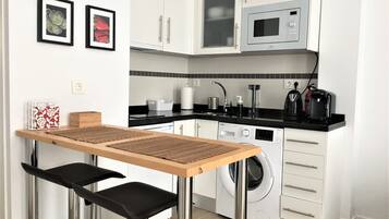 Una cocina compacta con armarios blancos, microondas, lavadora y un pequeño comedor con mesa y sillas.