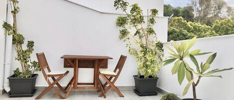 Een terras met een houten tafel en stoelen, omringd door potplanten.
