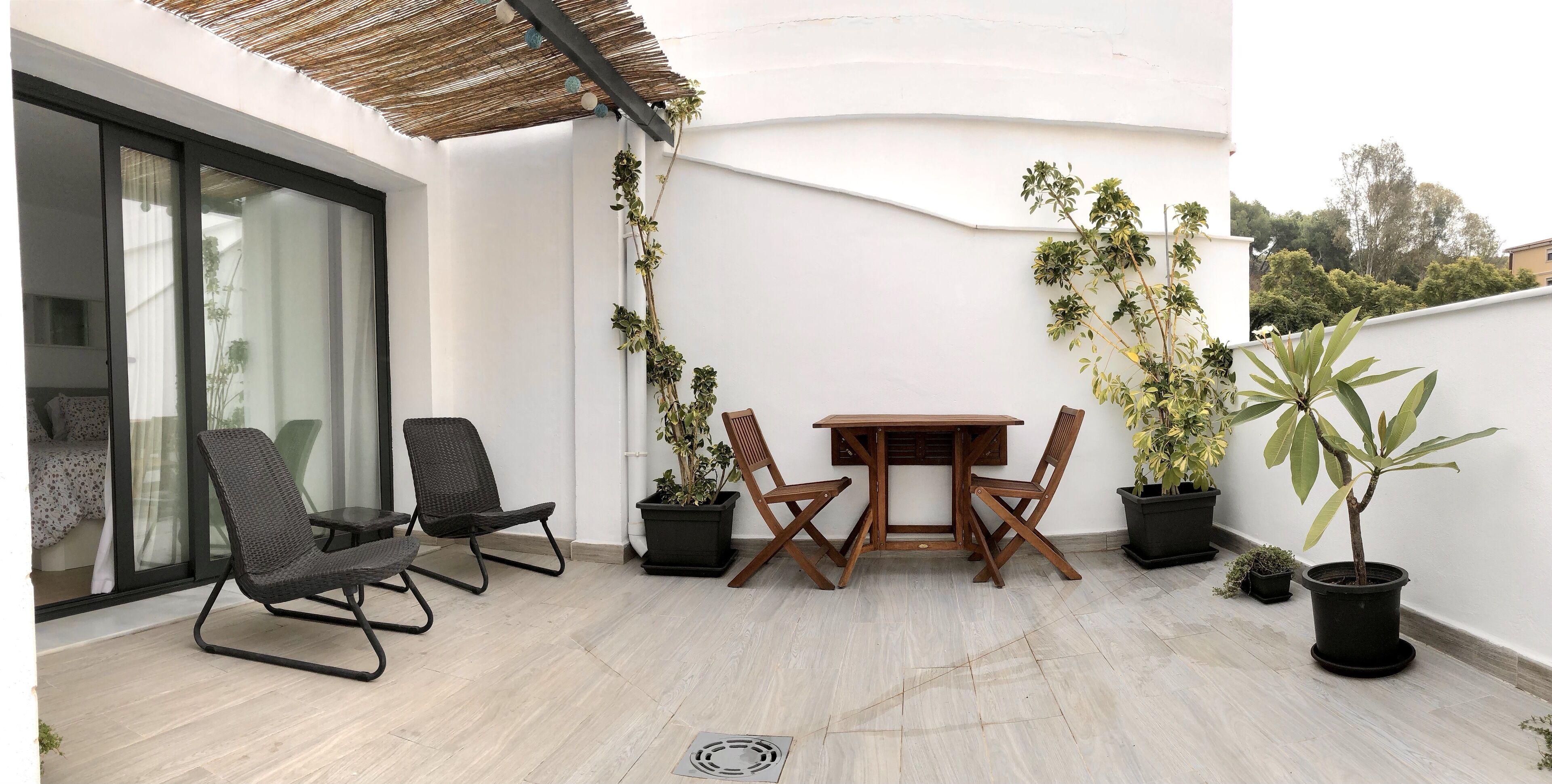 A balcony with a table and chairs, potted plants, and a view of the surrounding area.