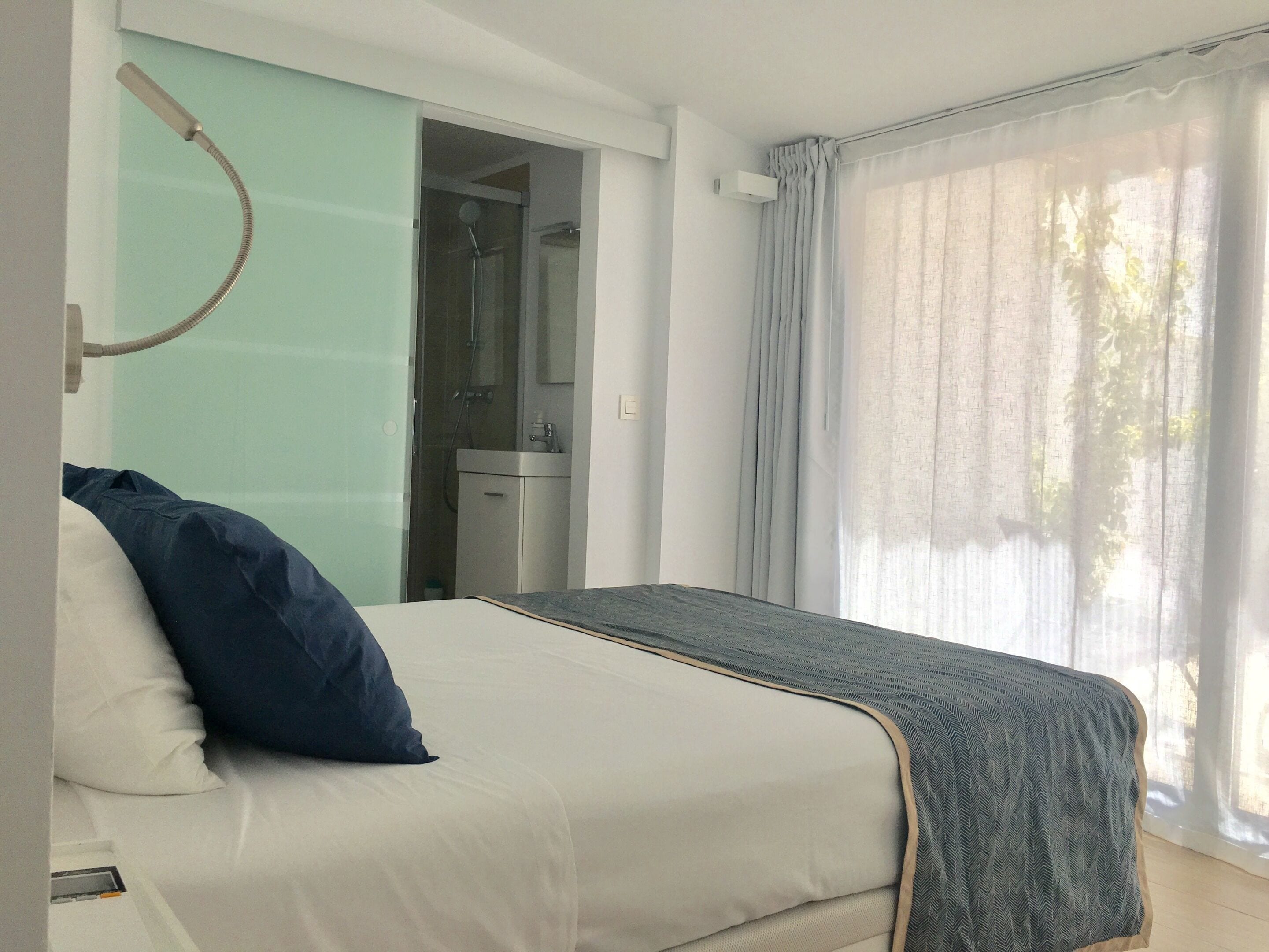 A bedroom with a bed, a bathroom with a shower, and a window with curtains.