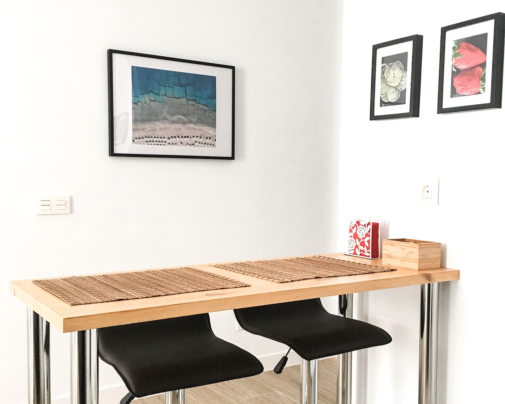 Una cocina moderna con encimera de madera, sillas negras y un cuadro enmarcado.