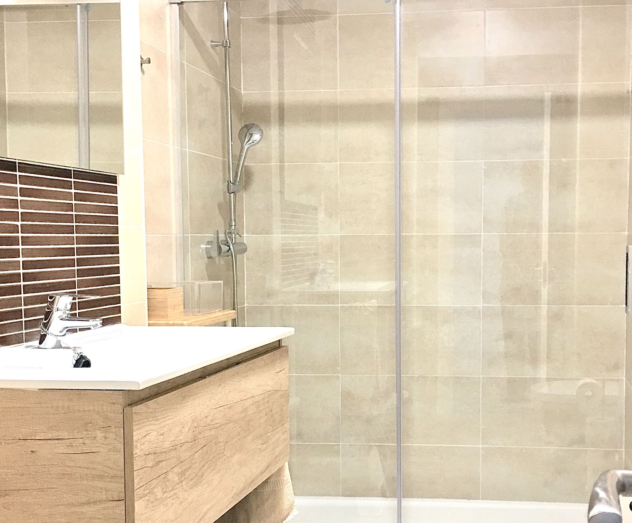 Une salle de bain avec un meuble-lavabo en bois, une cabine de douche en verre et un mur carrelé.