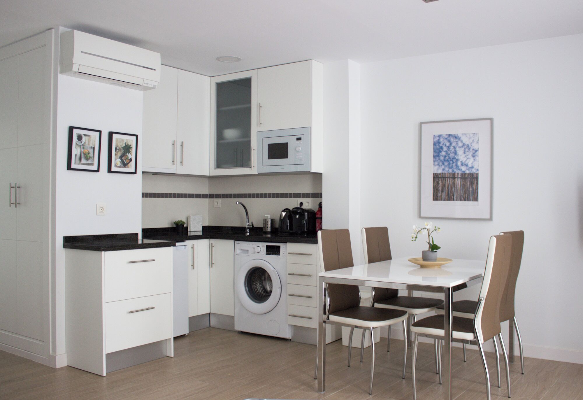 A modern kitchen with white cabinets, a built-in washing machine, and a dining area with a table and chairs.