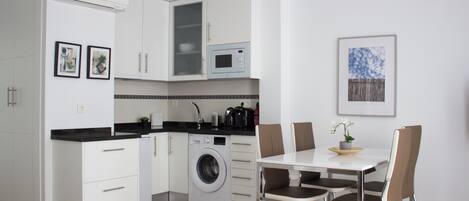A modern kitchen with white cabinets, a built-in washing machine, and a dining area with a table and chairs.