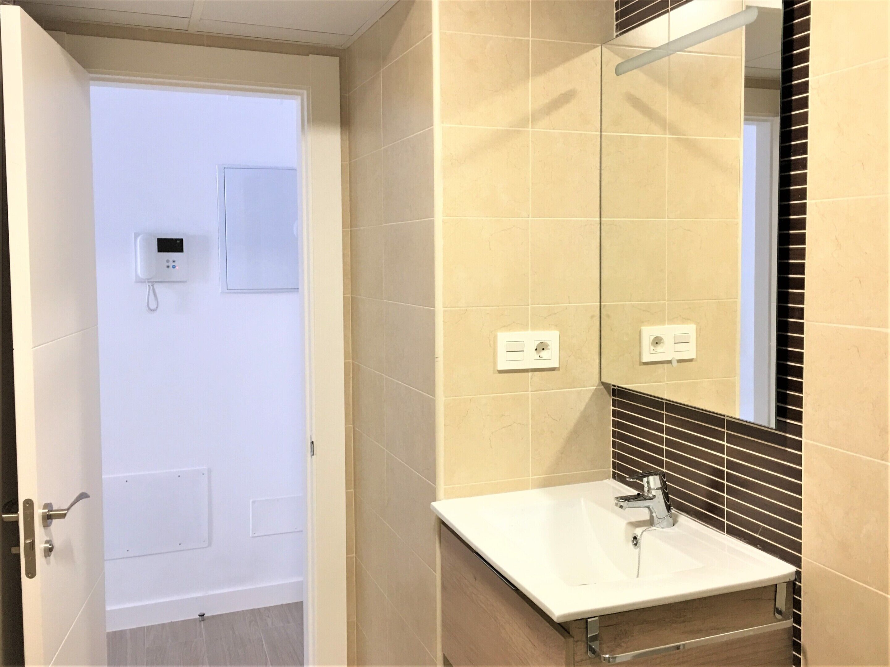 Un baño con lavamanos blanco, un espejo y una puerta con panel de control.