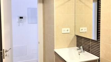 Un baño con lavamanos blanco, un espejo y una puerta con panel de control.
