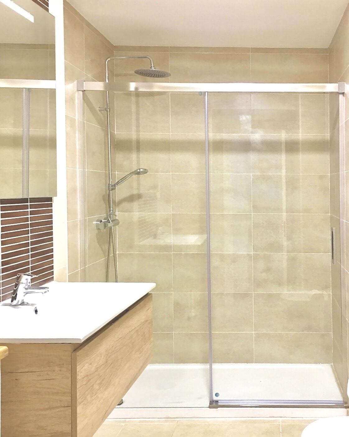 Ein modernes Badezimmer mit einer gläsernen Duschkabine, einem Holzkosmetikschrank und einem weißen Waschbecken.