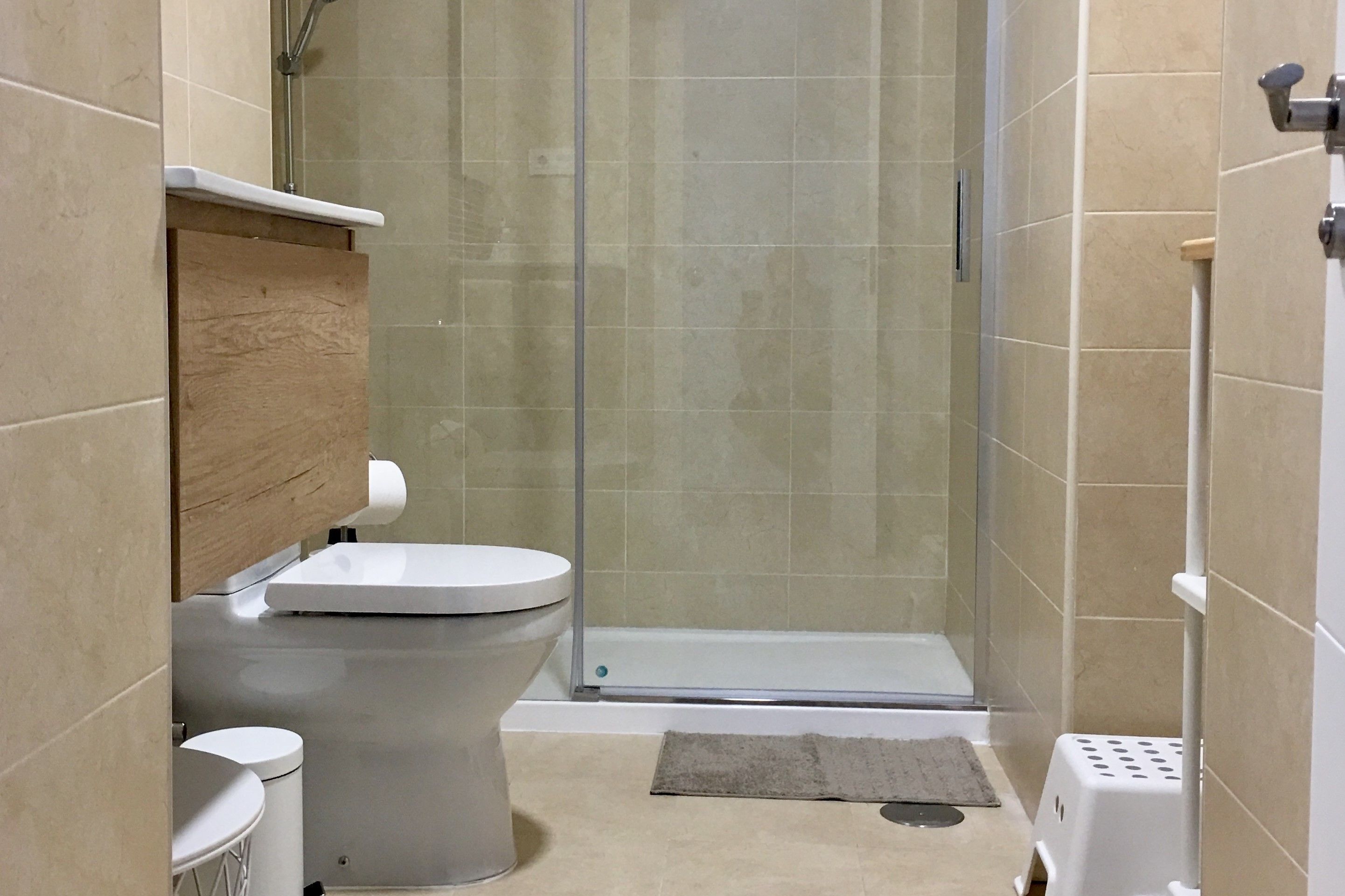 A modern bathroom with a toilet, a shower enclosure, and a small stool.