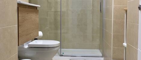 A modern bathroom with a toilet, a shower enclosure, and a small stool.