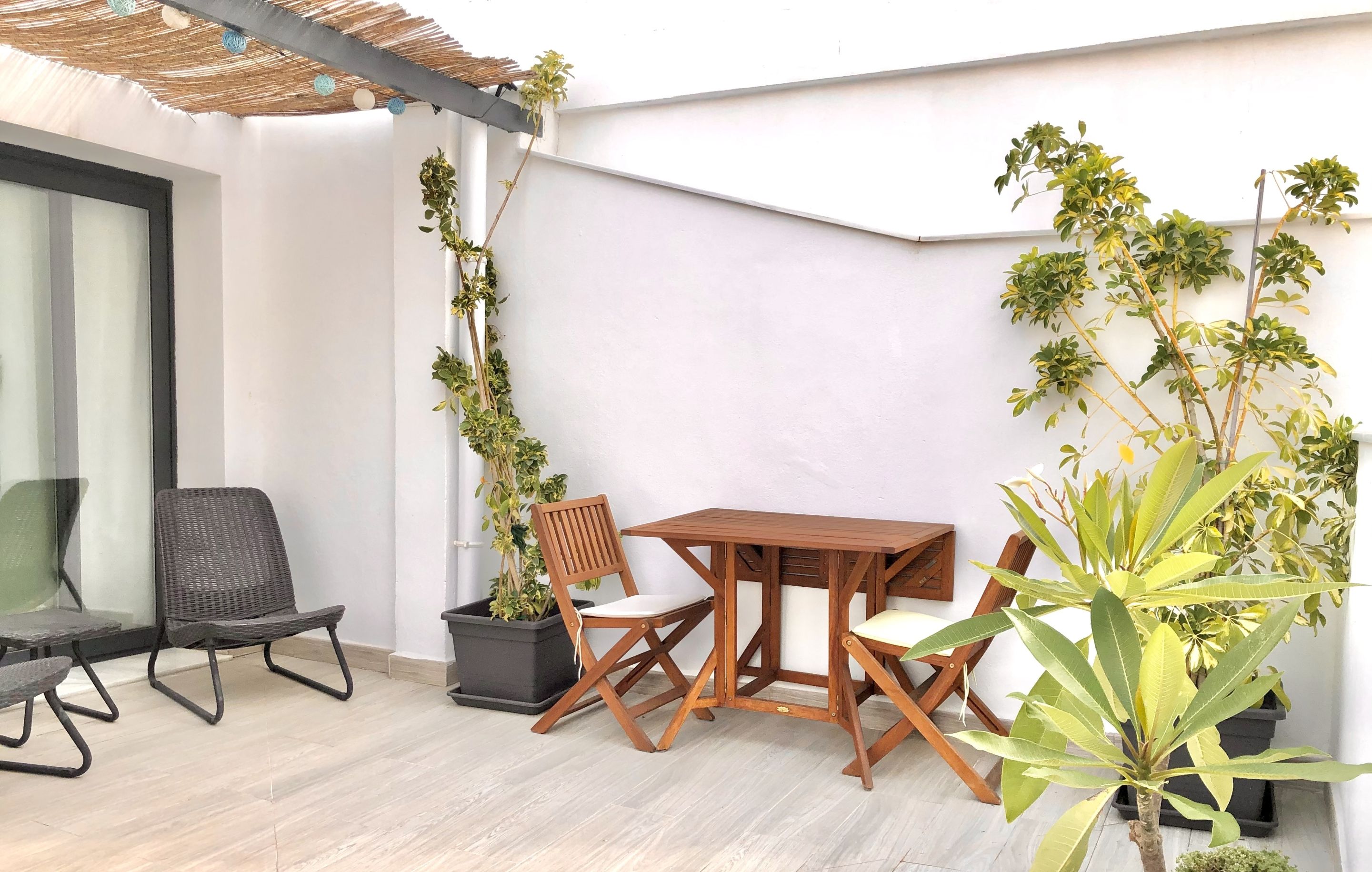 Une terrasse avec une table et des chaises en bois, entourée de plantes en pot.