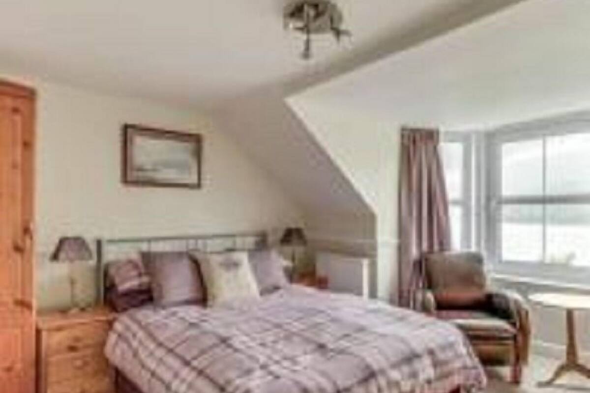 A bedroom with a bed, a nightstand, a chair, a window, and a wardrobe.