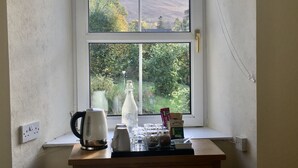 A room with a large window overlooking a mountainous landscape. Inside, there is a wooden table with a kettle, a bottle, and some jars. - TwoStones (Arrochar)
