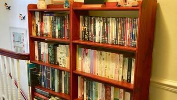 A bookshelf filled with books and DVDs, a framed sign above it, and a small figurine on top.