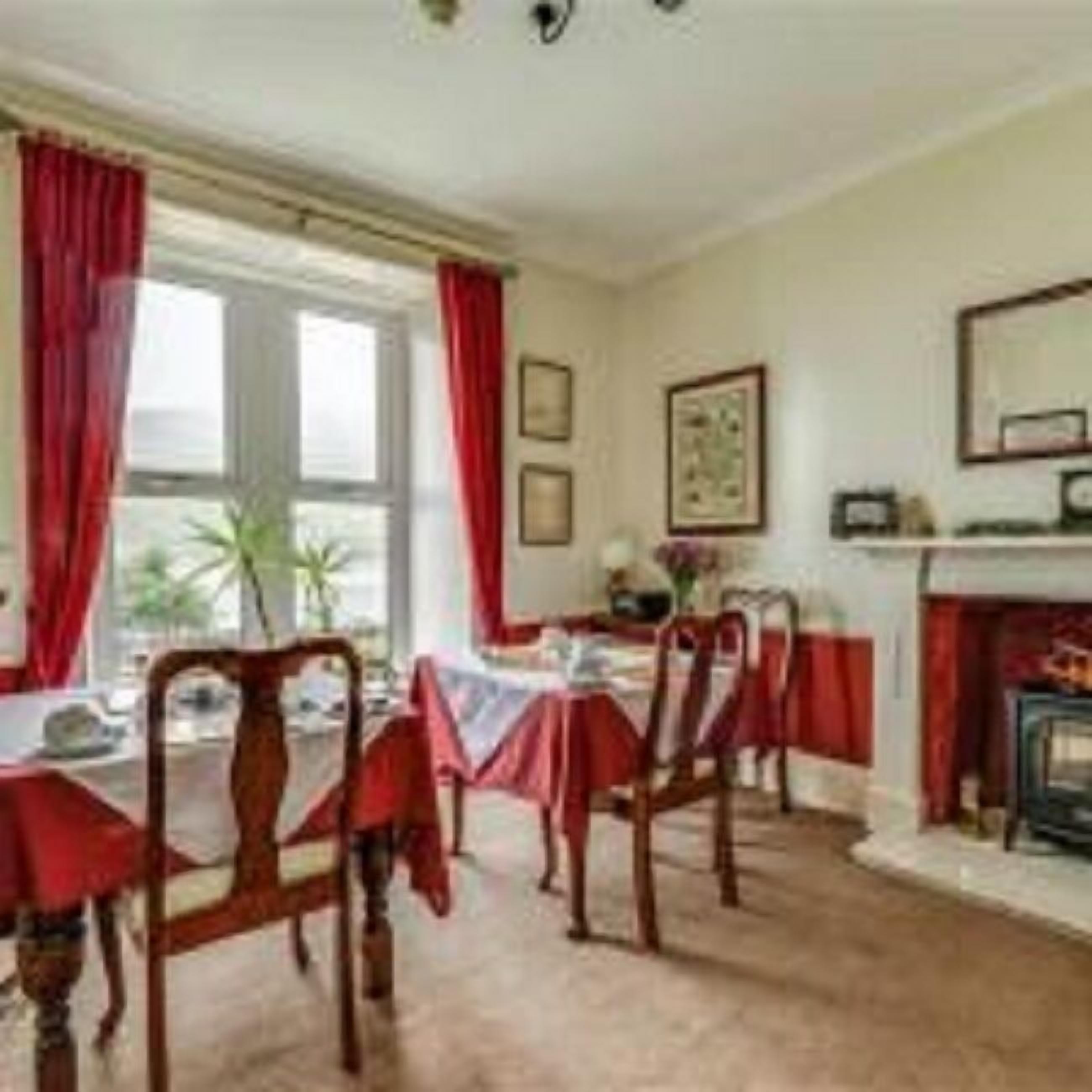 A dining room with a table set for four, red curtains, a fireplace, and framed pictures on the wall.