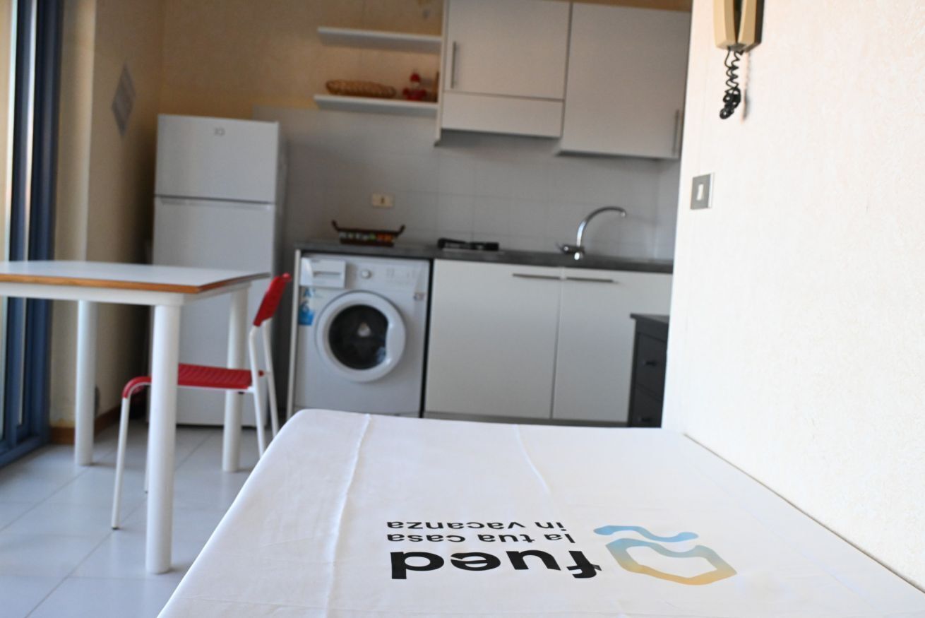 Cocina compacta con lavadora, un lavabo y una mesa con una silla.