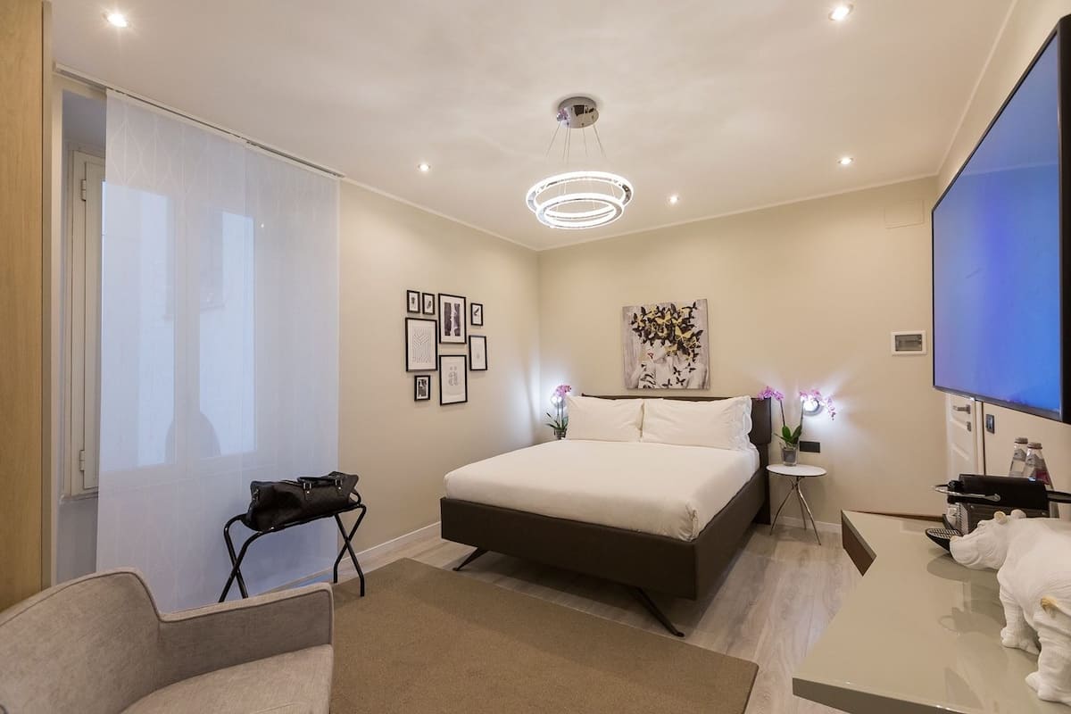 Una habitación de hotel moderna con una cama grande, un escritorio con televisor de pantalla plana, una mesita auxiliar pequeña y un área de baño con ducha e inodoro.