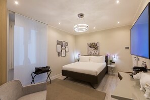 A modern hotel room with a large bed, a desk with a flat-screen TV, a small side table, and a bathroom area with a shower and toilet. - Clementi Portrait (Rome)
