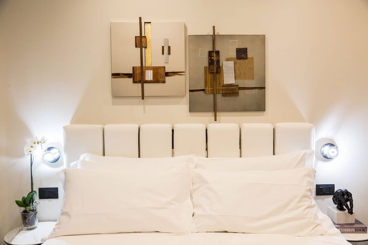 Un dormitorio moderno con un cabecero blanco, dos mesitas de noche con lámparas y arte abstracto en la pared.