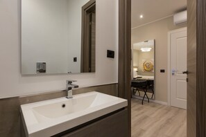 A modern bathroom with a large mirror, a white sink, and a wooden door. - Clementi Portrait (Rome)