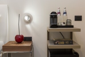 A modern room with a wooden side table, a red vase, a wall-mounted light, a shelf with bottles, a book, and a power outlet. - Clementi Portrait (Rome)