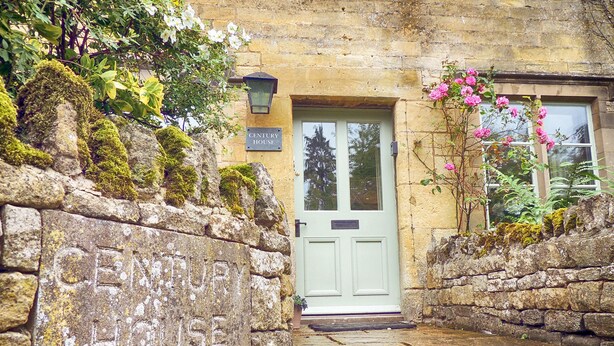 A stone wall with "CENTURY HOUSE" engraved, leading to a white door with a sign above it. - Century House (Moreton-in-Marsh)