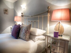 A neatly made bed with patterned pillows, a bedside lamp, and a nightstand with drawers. - Century House (Moreton-in-Marsh)