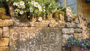 A stone wall with the inscription "CENTURY HOUSE" and a potted plant with purple flowers. - Century House (Moreton-in-Marsh)