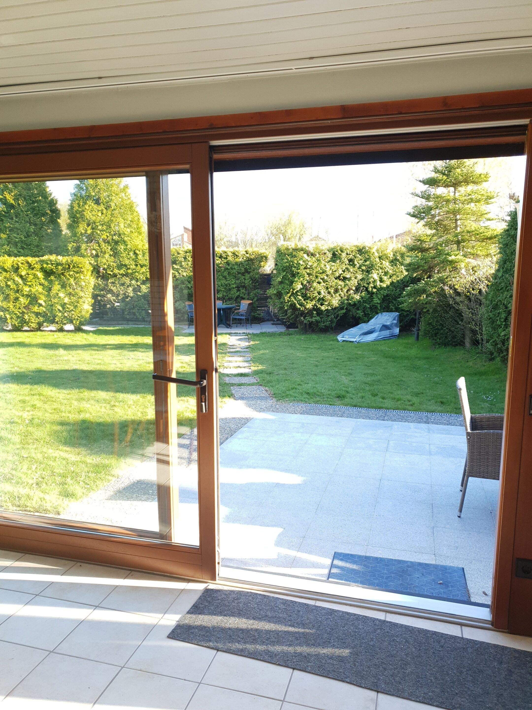 A sliding glass door leading to a patio with a lawn, a chair, and a small table.