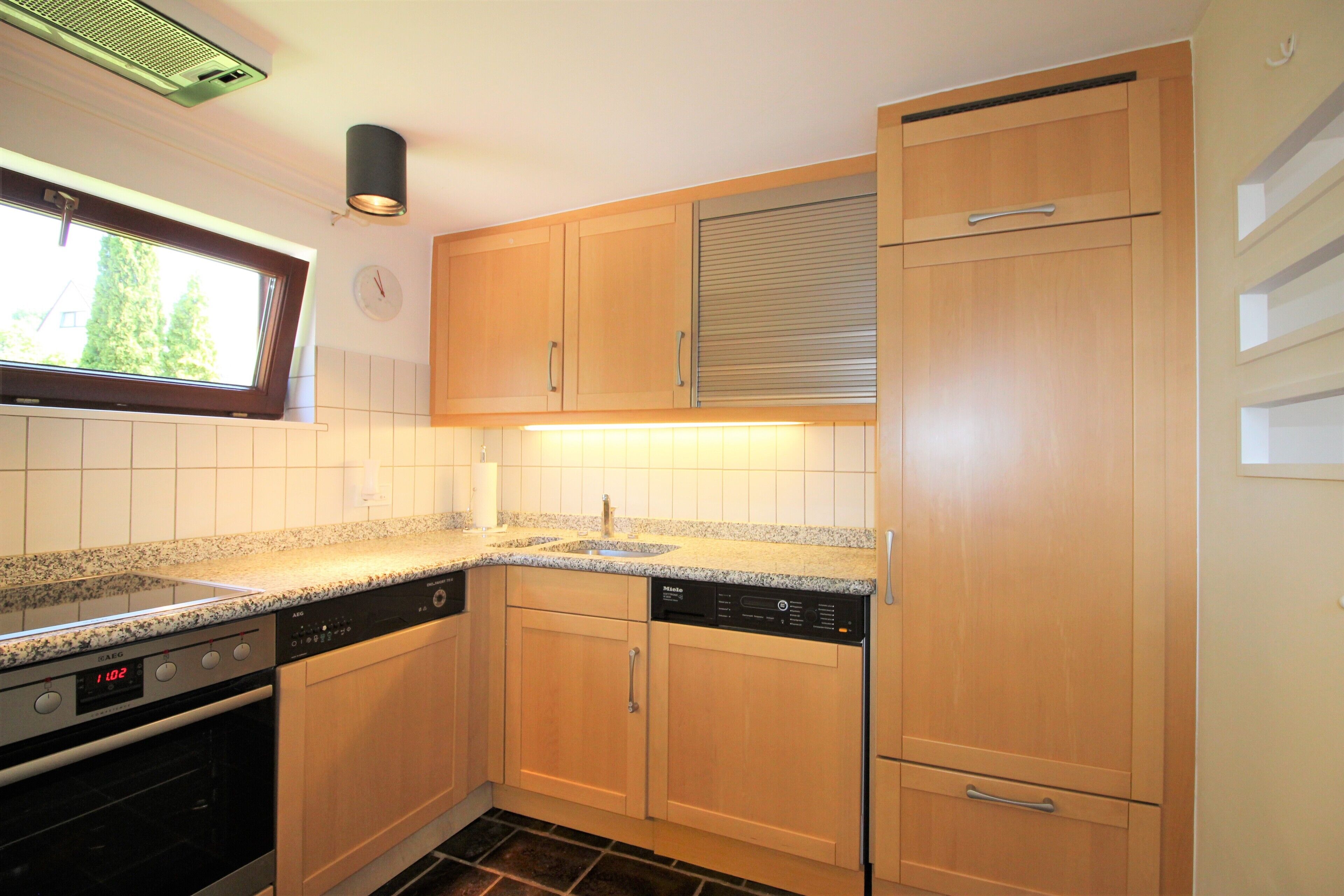 A kitchen with wooden cabinets, a dishwasher, an oven, and a window with blinds.