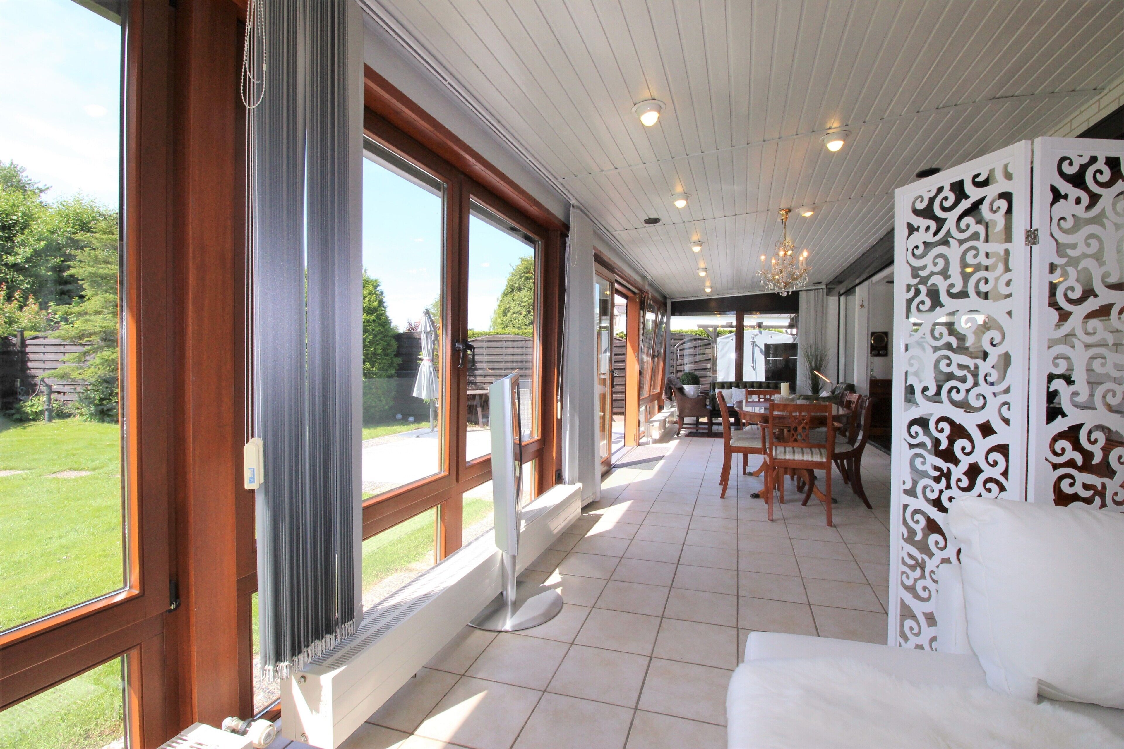 A spacious room with large windows, a white sofa, and a dining area with wooden furniture.