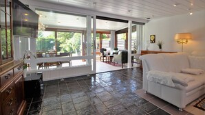 A spacious living area with a white sofa, a dining table, and a kitchen area with a TV and cabinets. - Bay of Lübeck, Scharbeutz, holiday house 50 m to the beach (Scharbeutz)