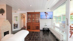 A spacious living room with a fireplace, a large wooden cabinet, a television, and a view of the outdoors. - Bay of Lübeck, Scharbeutz, holiday house 50 m to the beach (Scharbeutz)
