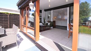 A modern house with a patio area featuring wicker furniture and a glass door leading to a kitchen with a dining table and chairs. - Bay of Lübeck, Scharbeutz, holiday house 50 m to the beach (Scharbeutz)