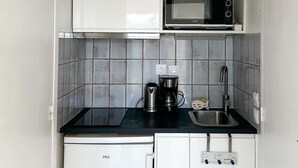 A compact kitchen with white cabinets, a microwave, a coffee maker, and a sink.
