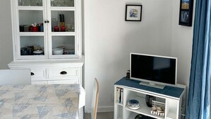 A room with a dining table, a white cabinet with glass doors, a television on a stand, and framed pictures on the wall.