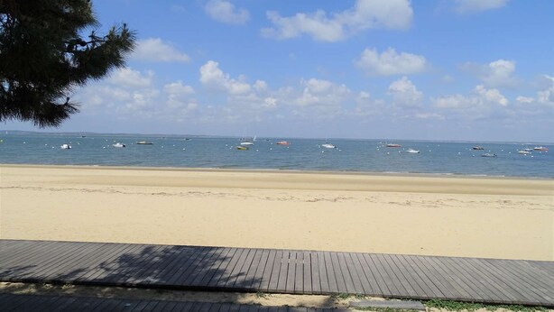 A beach with a wooden boardwalk leading to the water, where several boats are anchored.