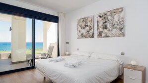 A bedroom with a large bed, a nightstand, and a chair by a sliding glass door leading to a balcony with a view of the sea. - The Links I 2226 Golf & Sea views (La Alcaidesa)