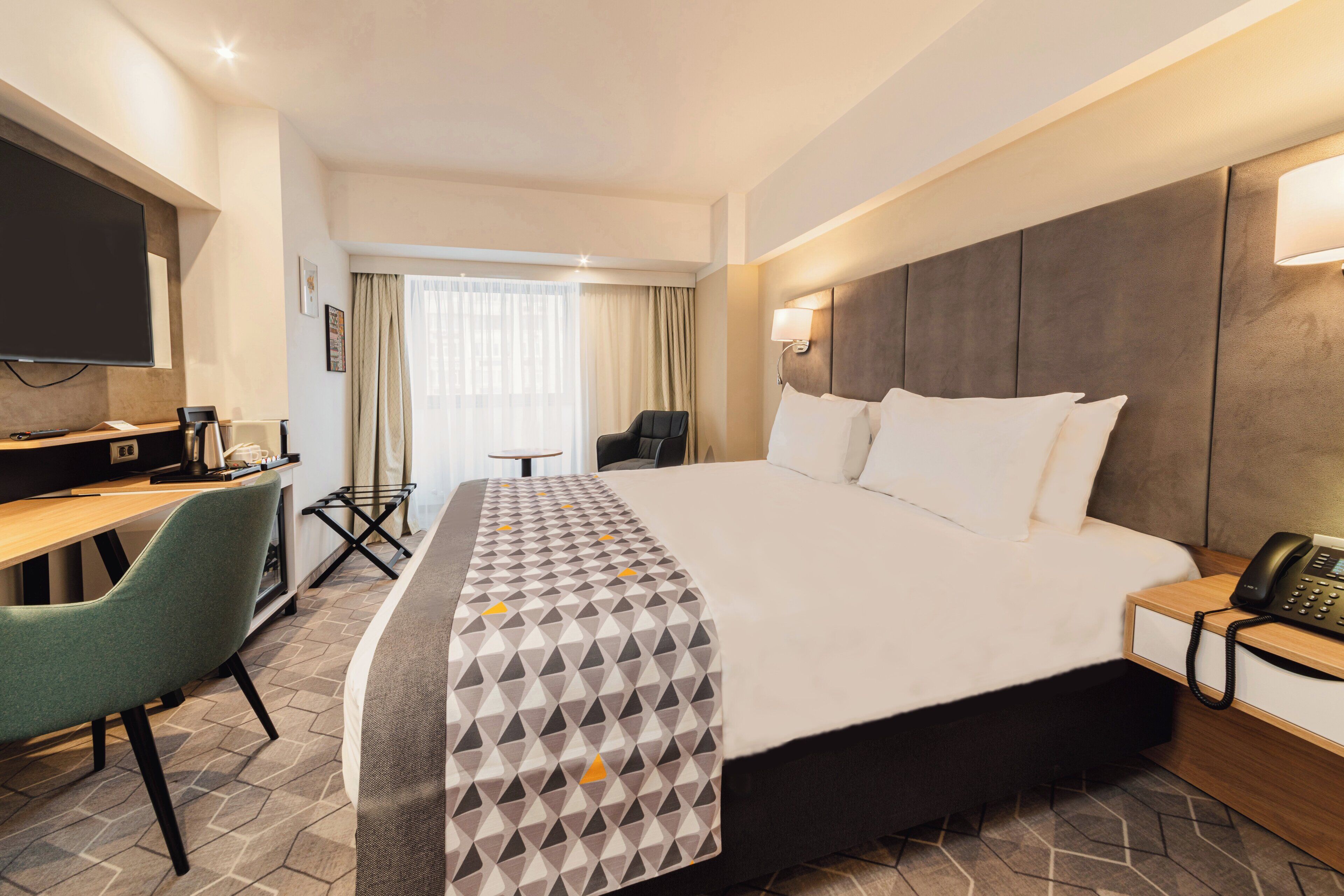 A hotel room with a large bed, a desk with a chair, a television, and a telephone.