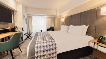 A hotel room with a large bed, a desk with a chair, a television, and a telephone.